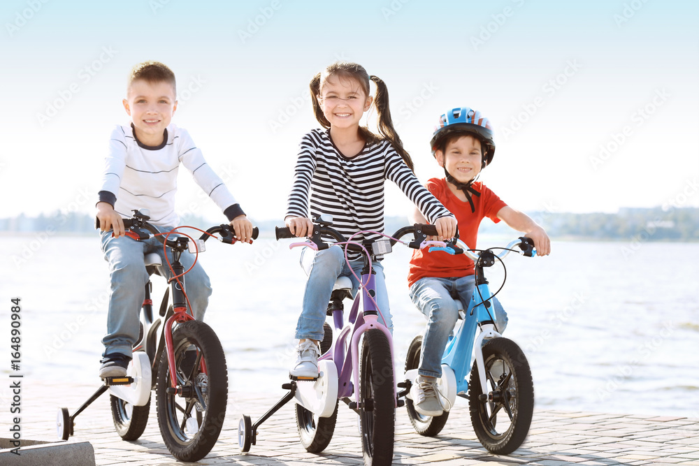 Cute little children riding bicycles near river on sunny day