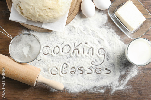 Text written on flour and ingredients, wooden background. Cooking classes concept