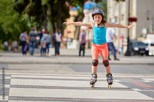 Funny Little pretty girl on roller skates in helmet riding in a park.