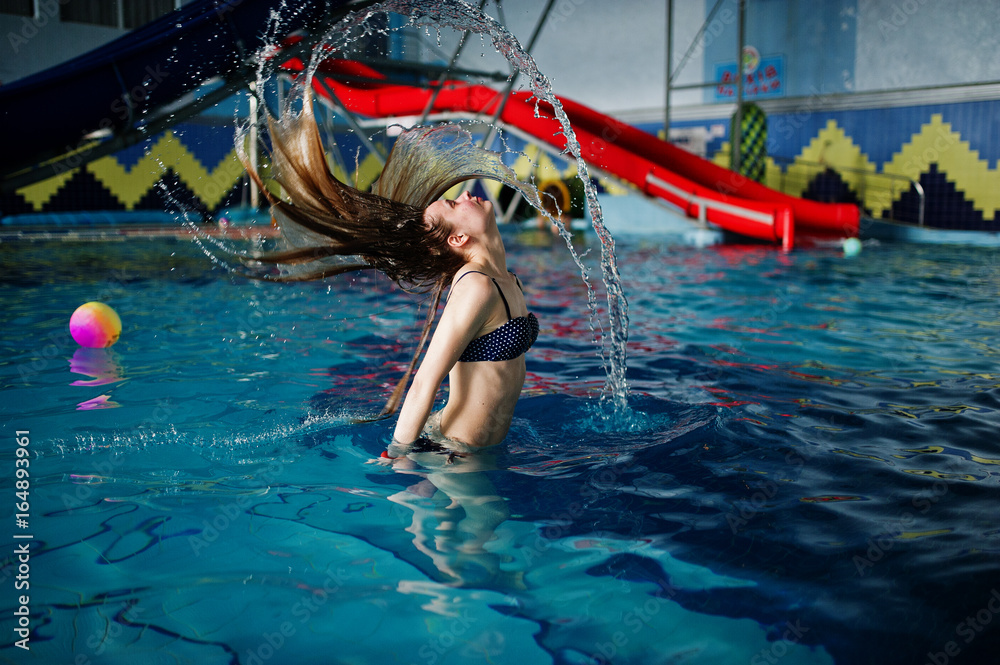 Portrait of a gorgeous firl in bikini making a splash with her hair in the pool in water park.