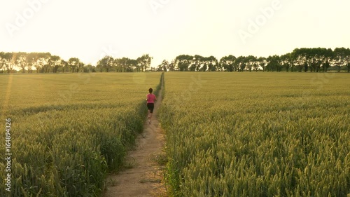 4K video clip of beautiful healthy mixed race African American girl teenager female young woman runner running on path through field of barley or wheat crops at sunset