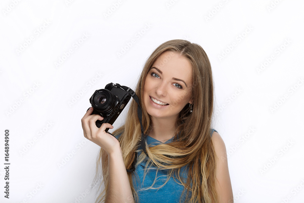 Headshot of young adorable playful blonde woman with cute smile in cobalt color blouse posing with black dslr camera on white backdrop