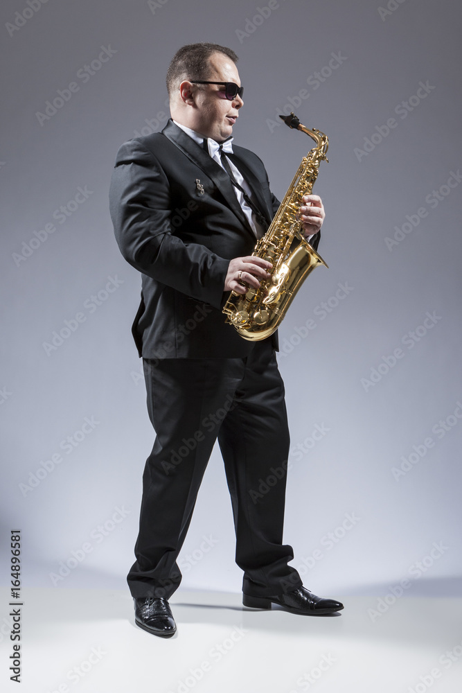 Fototapeta premium Music Ideas and Concepts. Full Length Portrait of Caucasian Saxophone Player in Sunglasses Playing the Instrument in Studio Environment.