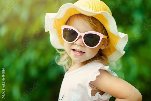 Pretty little girl in a striped dress and hat relaxing on the beach near sea, summer, vacation, travel concept. smiling cute little girl on beach vacation. Baby girl in hat and sun glasses on beach