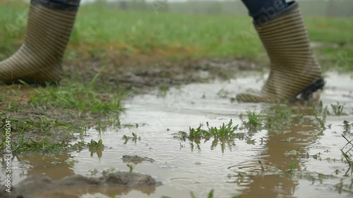 Person with pink boots and blue umbrella splashing in the puddle. girl in raincoat and rubber boots jumping into puddle. rubber boots comes in a puddle photo