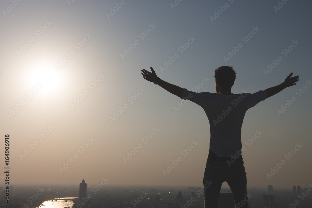 Man standing at the edge of rooftop, stretching arms. Sunset on cityscape background Freedom or success concept. Copy space.