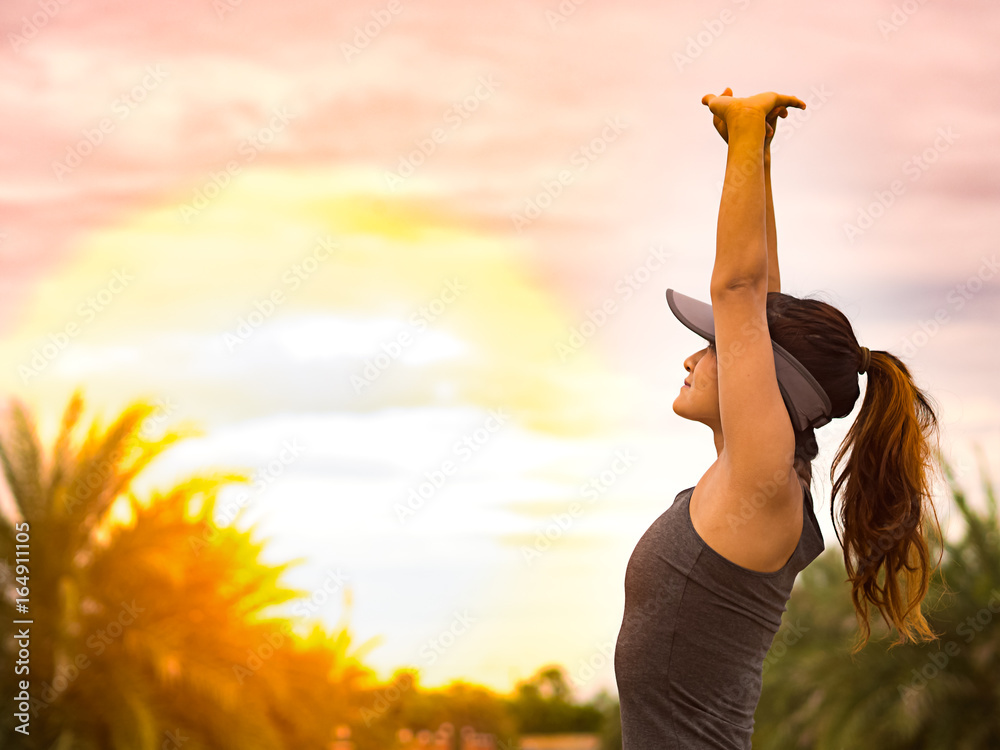 Woman runner stretching arms before running on sunrise background in morning, upper body of happy female athlete