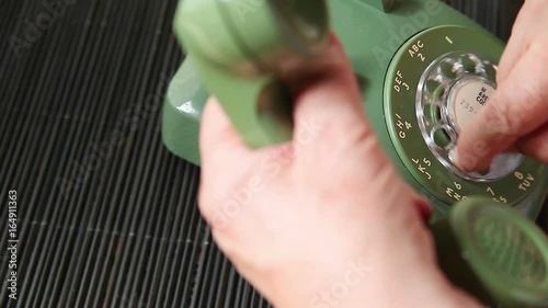 A senior man holds the handset while dialing an old rotary phone with room for text