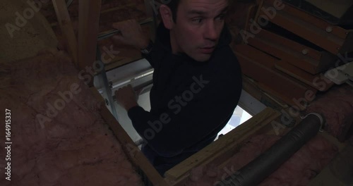Male climbing attic ladder and searching through stored boxes photo