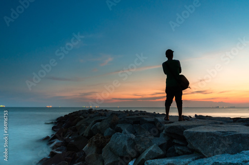 Silhouette man standing on the beach side enjoy sunset view 