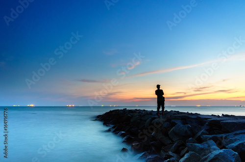 Silhouette man standing on the beach side enjoy sunset view 