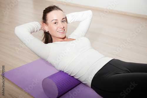attractive girl coach demonstrates exercises myofascial relaxation on the foam roller