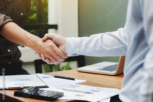 Close-up of two business executives shaking hands with data documents on the table