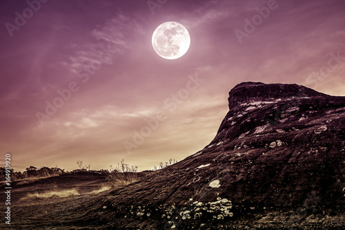 Landscape of rock against sky and full moon above wilderness area in forest.