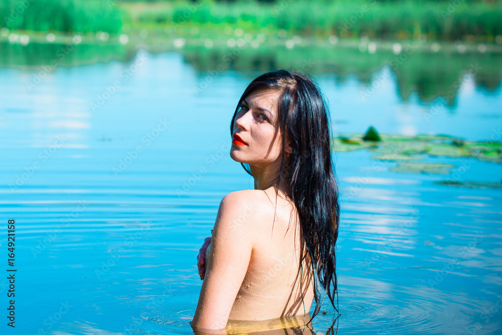 Mermaid girl with dark hair on a blue lake. Sexy and thin figure, red lids and pale skin. Inspire woman bathed in water and seduces