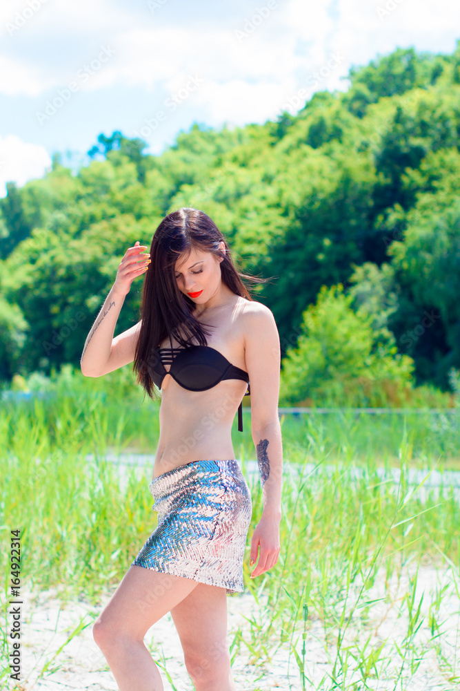 Young beautiful woman rest on a nature outdoors in glitter skirt and swimwear. Good mood and having fun on a sunny day Young beautiful woman rest on a nature outdoors in glitter skirt and swimwear. Good mood and having fun on a sunny day