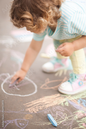 Cute toddler girl drawing with piece of color chalk