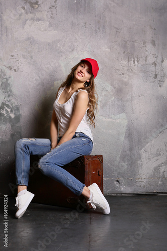 Smiling young woman sitting on suitcase, before travel, indoor, positive