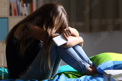 Sad teen with a phone in her bedroom