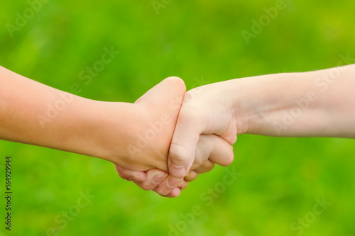 Gesture of handshake of boys on a blurred green background. Toned © watman