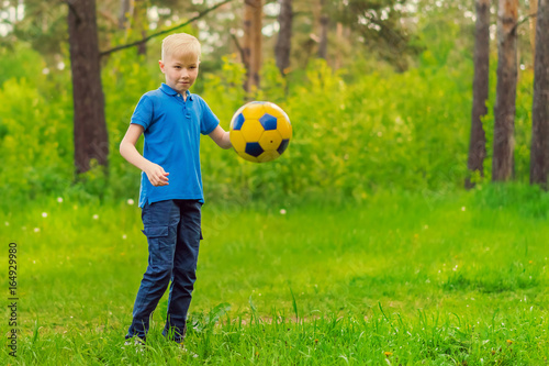 Blond boy in a blue T-shirt kicking soccer ball in the park
