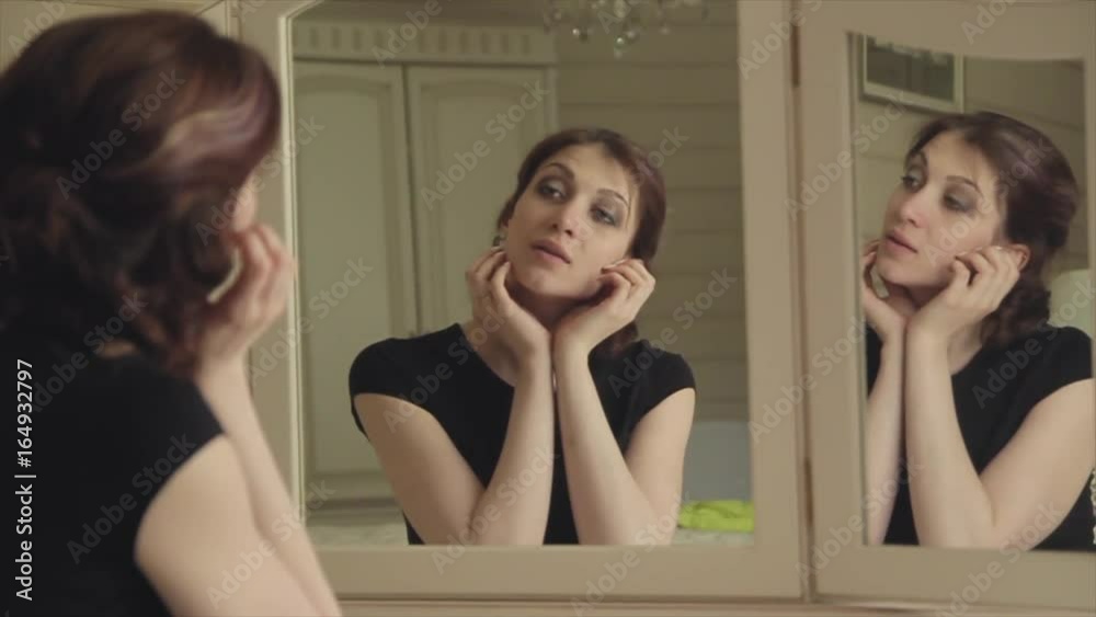 Beautiful young girl in a black dress sits in front of a vintage mirror, reflected in three mirrors Beautiful young girl in a black dress sits in front of a vintage mirror, reflected in three mirrors