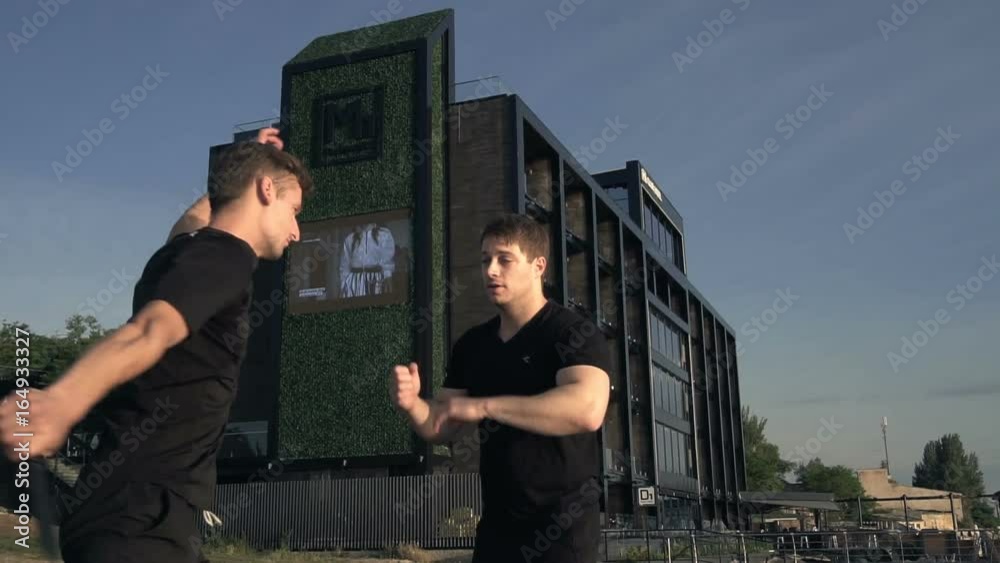Two young men with knife fight training against sunrise in slow motion