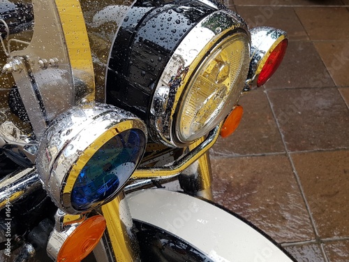 Red and blue emergency lights mounted on the front of a police motorcycle covered in water droplets
