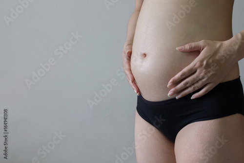 Woman are pregnant on gray background. The abdominal section of the womb. Pregnancy is about 5 months.