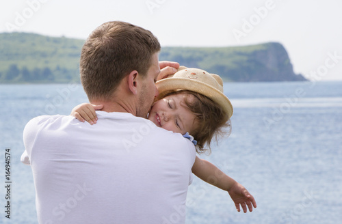 Dad kisses his daughter. Little girl with hat hugs father