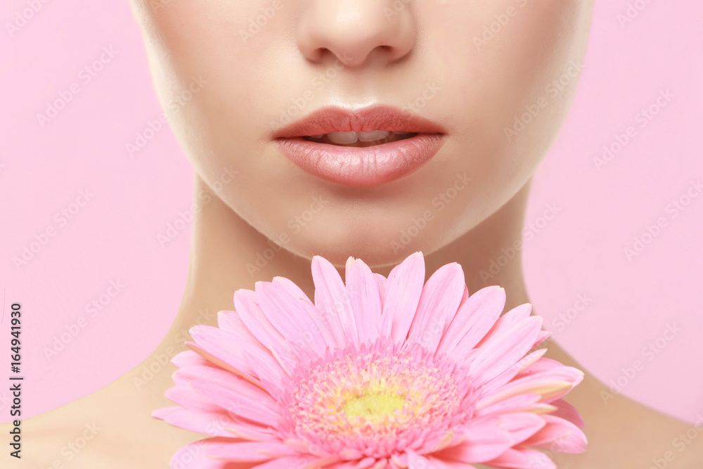 Closeup view of beautiful young woman with natural lips makeup and flower on color background Closeup view of beautiful young woman with natural lips makeup and flower on color background