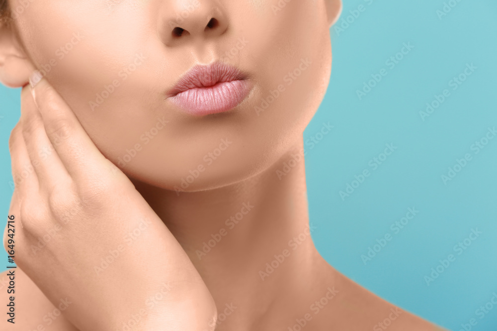 Closeup view of beautiful young woman with natural lips makeup touching neck on color background Closeup view of beautiful young woman with natural lips makeup touching neck on color background