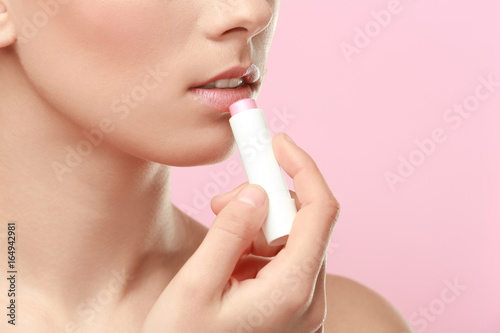 Closeup view of beautiful young woman applying lipstick  color background