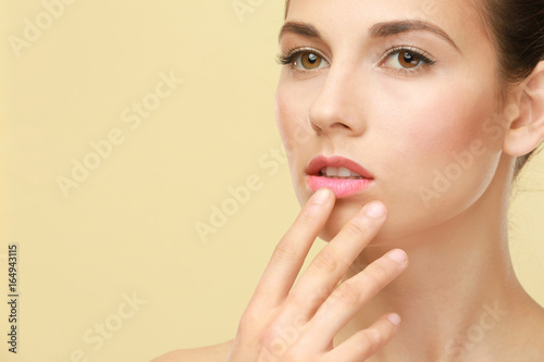 Closeup view of beautiful young woman with natural makeup touching lips on color background