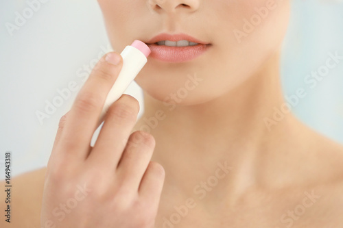 Closeup view of beautiful young woman applying lipstick  light background