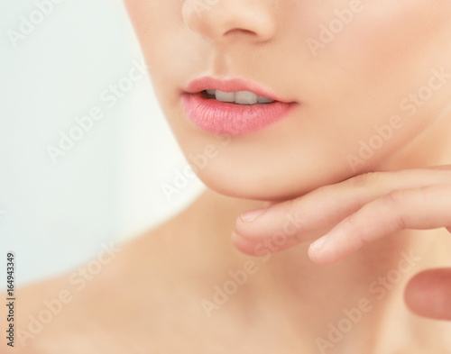 Closeup view of beautiful young woman with natural lips makeup touching face on light background