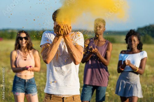 young multiethnic friends blowing powder from palms at holi festival