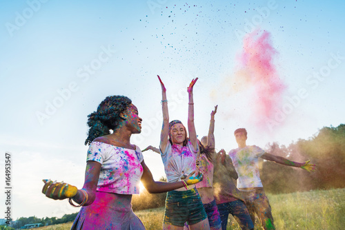 happy young multiethnic friends throwing colorful powder at holi festival