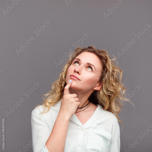 Blonde woman looking up touching chin