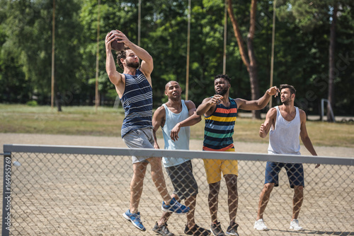 group of young multicultural men playing football on court