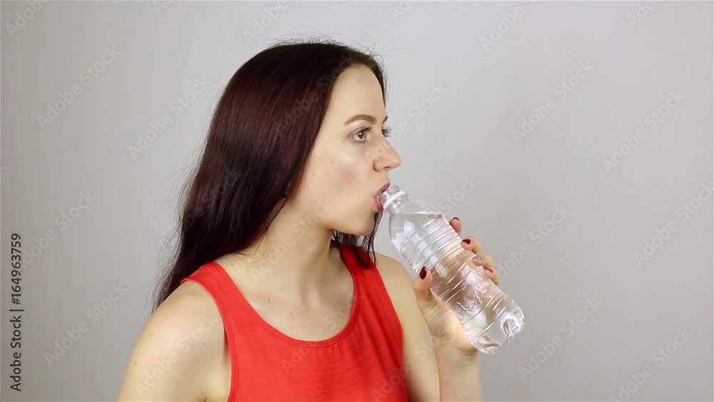 Beautiful young woman opens a bottle and drinks water Beautiful young woman opens a bottle and drinks water