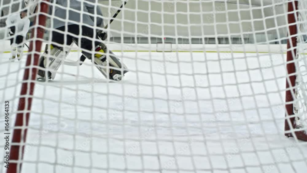 PAN from behind net of hockey goalie guarding net, then performing
