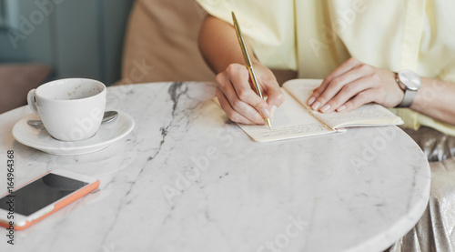 Hands of cropped unrecognisable woman writing in her notebook on coffee table. photo