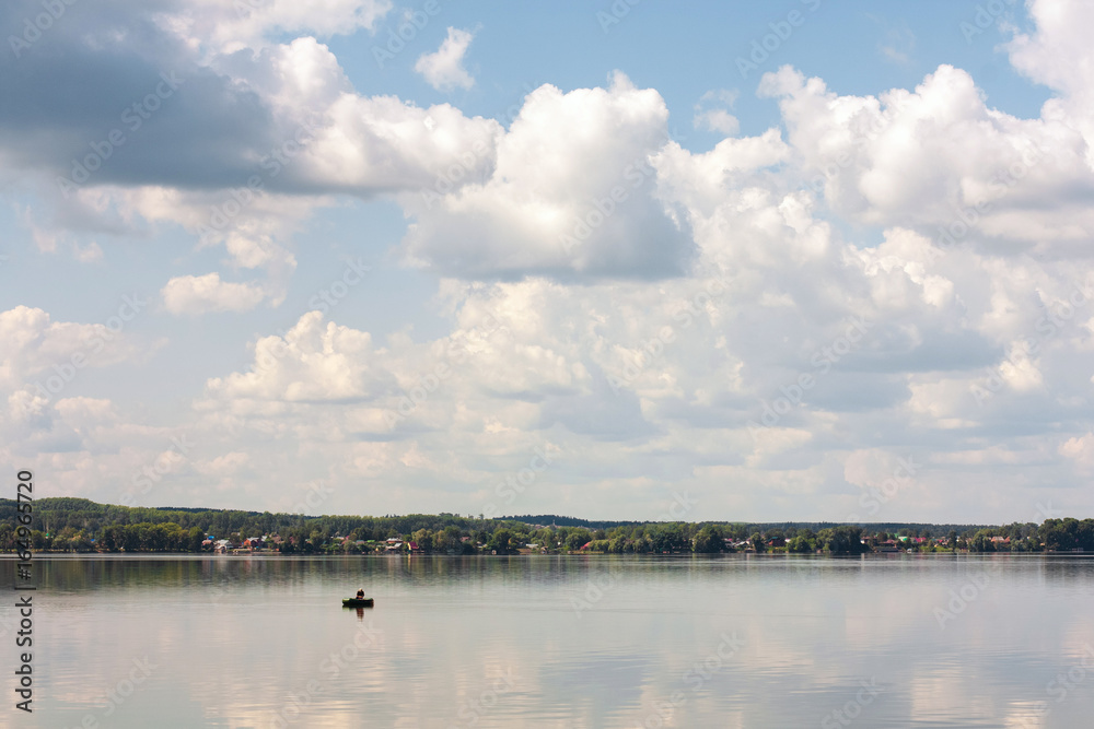 Fisherman in a rubber boat on the river. Russian landscape. Reflection of the sky in the pond Fisherman in a rubber boat on the river. Russian landscape. Reflection of the sky in the pond