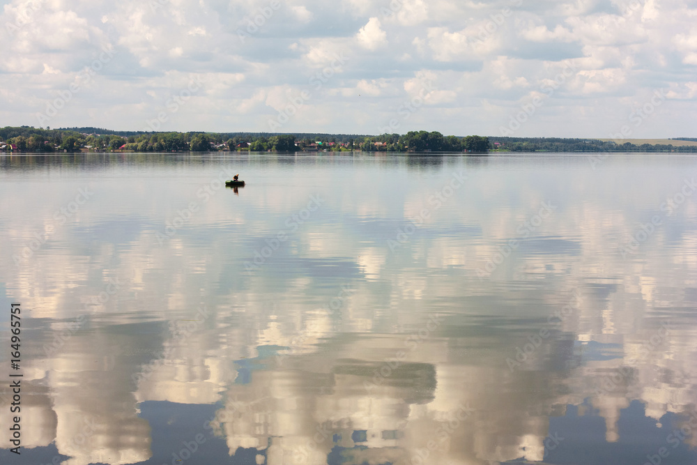 Fisherman in a rubber boat on the river. Russian landscape. Reflection of the sky in the pond