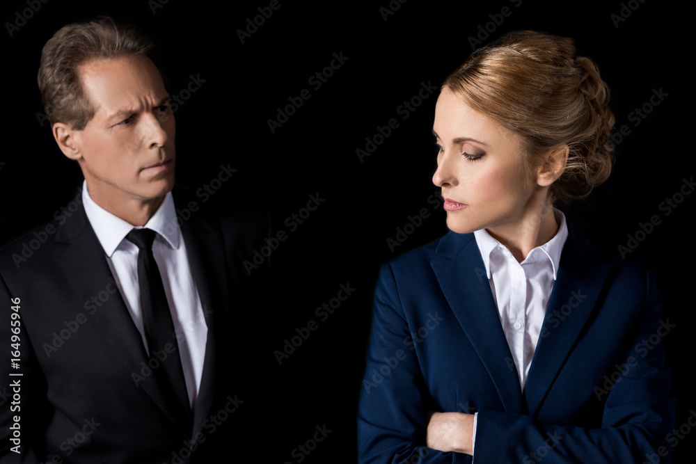 serious middle aged businesswoman standing with crossed arms and looking at colleague isolated on black serious middle aged businesswoman standing with crossed arms and looking at colleague isolated on black