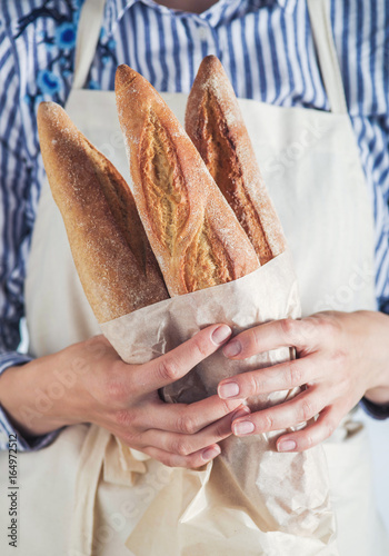 Close-up image of woman holding package of fresh baguettes.