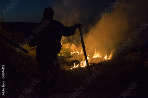 man silhouette standing in front of a fire and leaning on a bracket during the night.