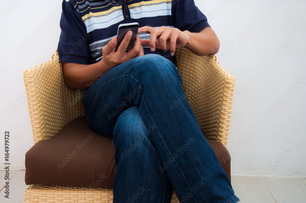 Smart young man using his smart phone while sitting on the chair in the room. texting