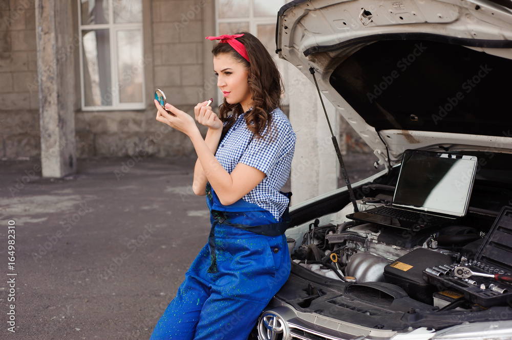 Fototapeta premium Cute attractive girl examining car engine at the auto repair shop